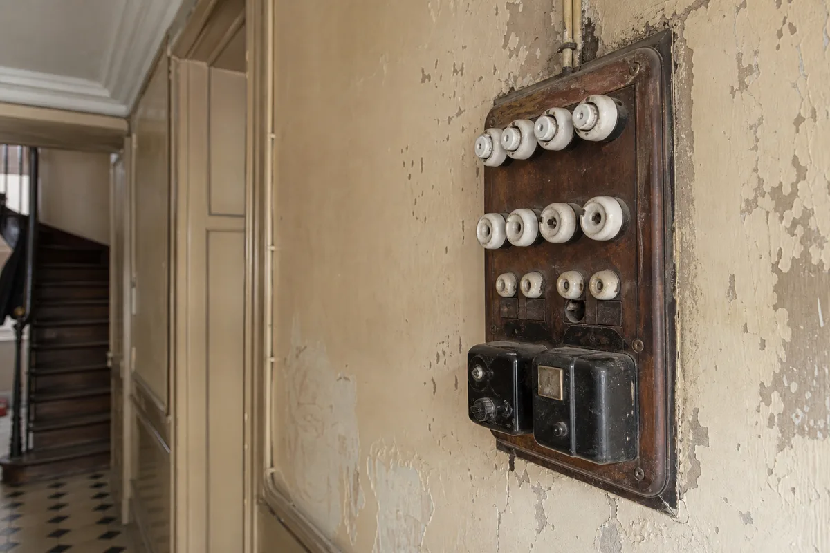 Vieux tableau électrique à fusibles porcelaine fixé sur un mur défraîchi dans un immeuble ancien du 20e