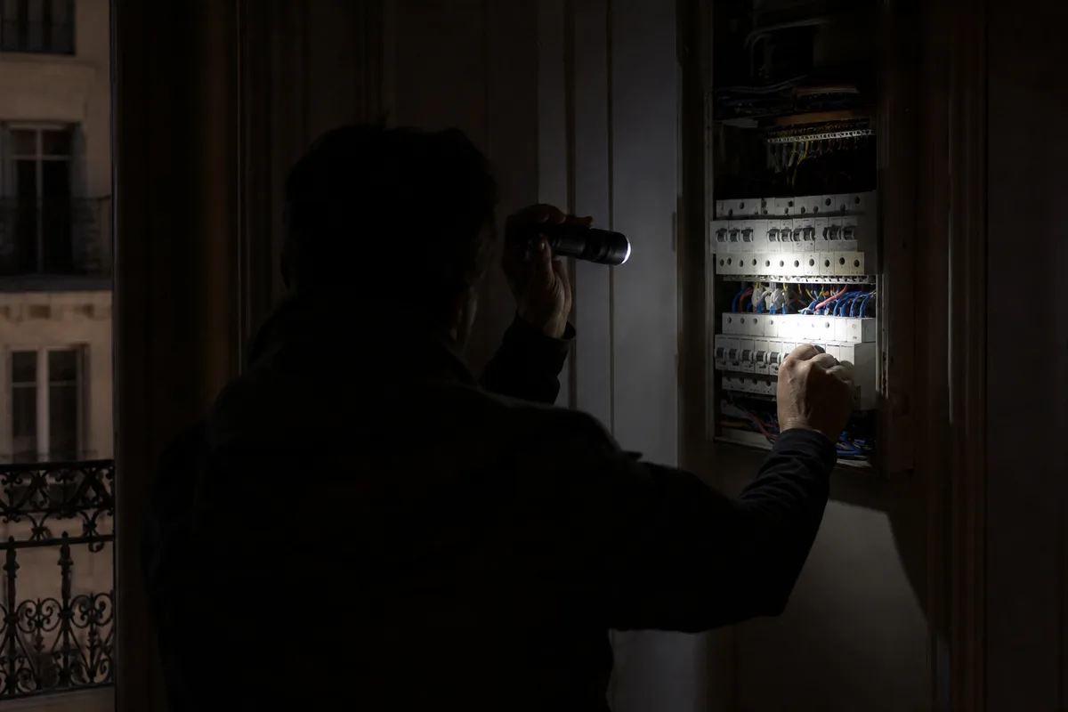 Inspection à la lampe torche d&rsquo;un tableau électrique dans un appartement parisien plongé dans le noir
